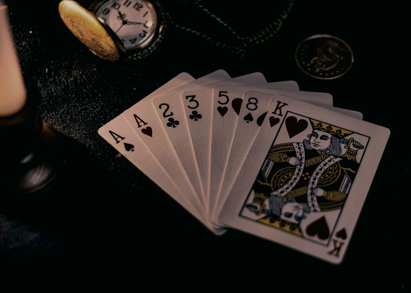 A fanned poker hand beside a pocket watch, low-light